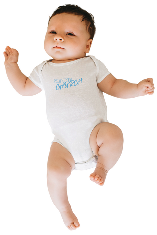 Baby wearing a white onesie with 'We The Church' text centre chest, lying on a white bed.